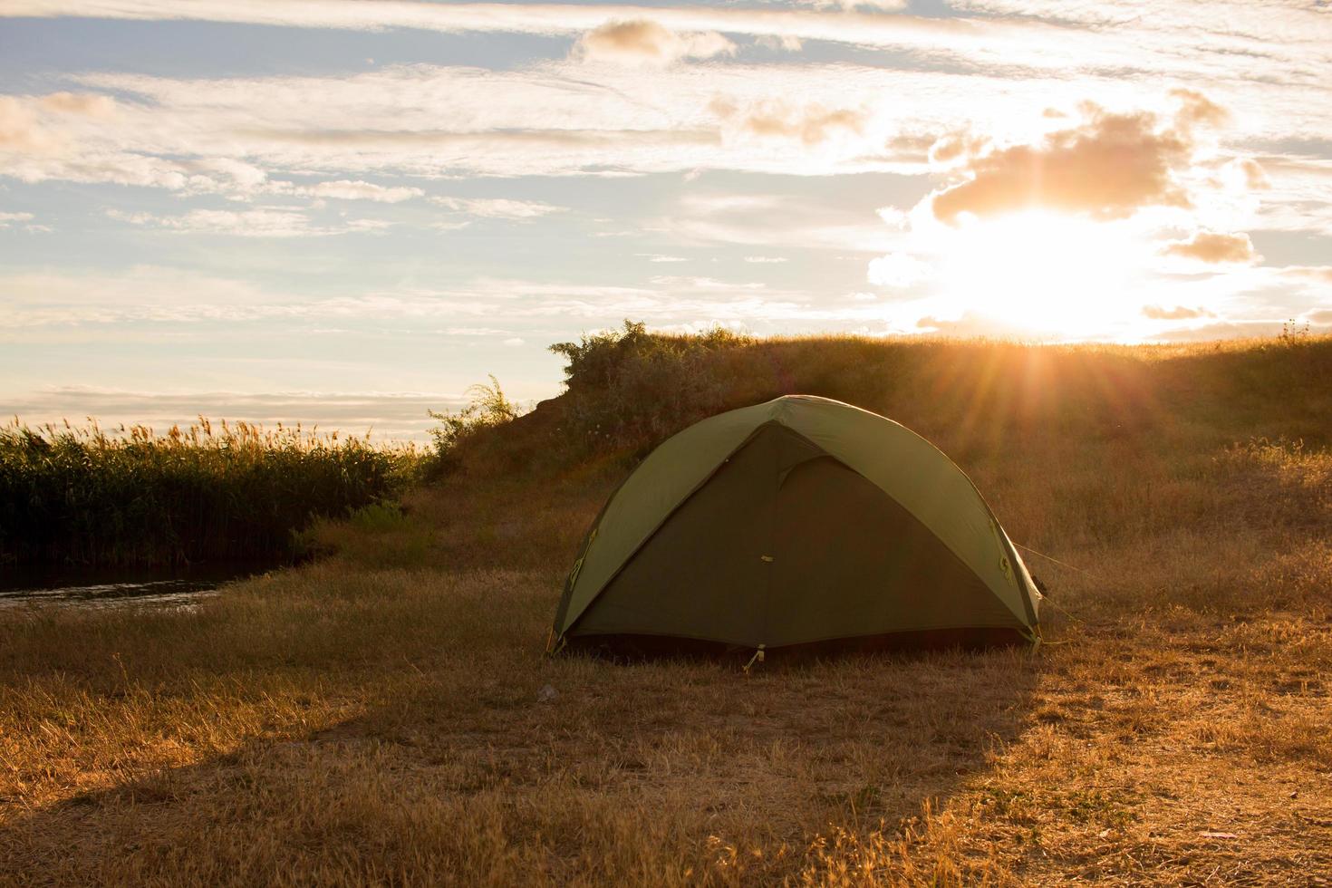 Grünes Zelt von Wanderern in der Nähe des Flusses während des Sonnenuntergangs oder Sonnenaufgangs foto