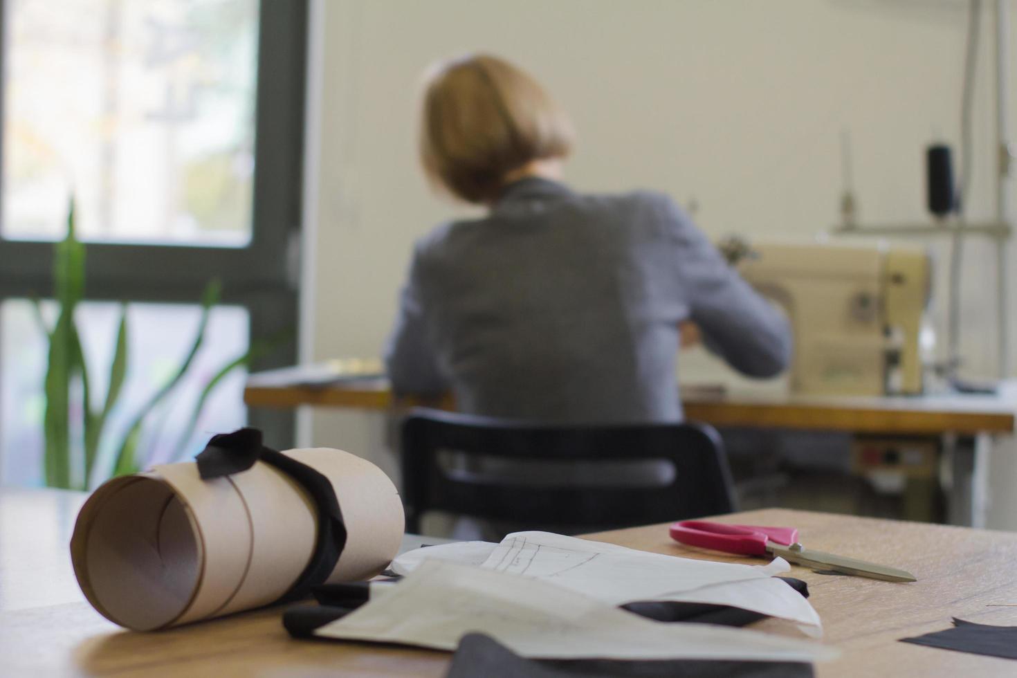 Näherin bei der Arbeit auf dem Tisch, Schneiderfrau arbeitet im Studio mit Kleidung foto