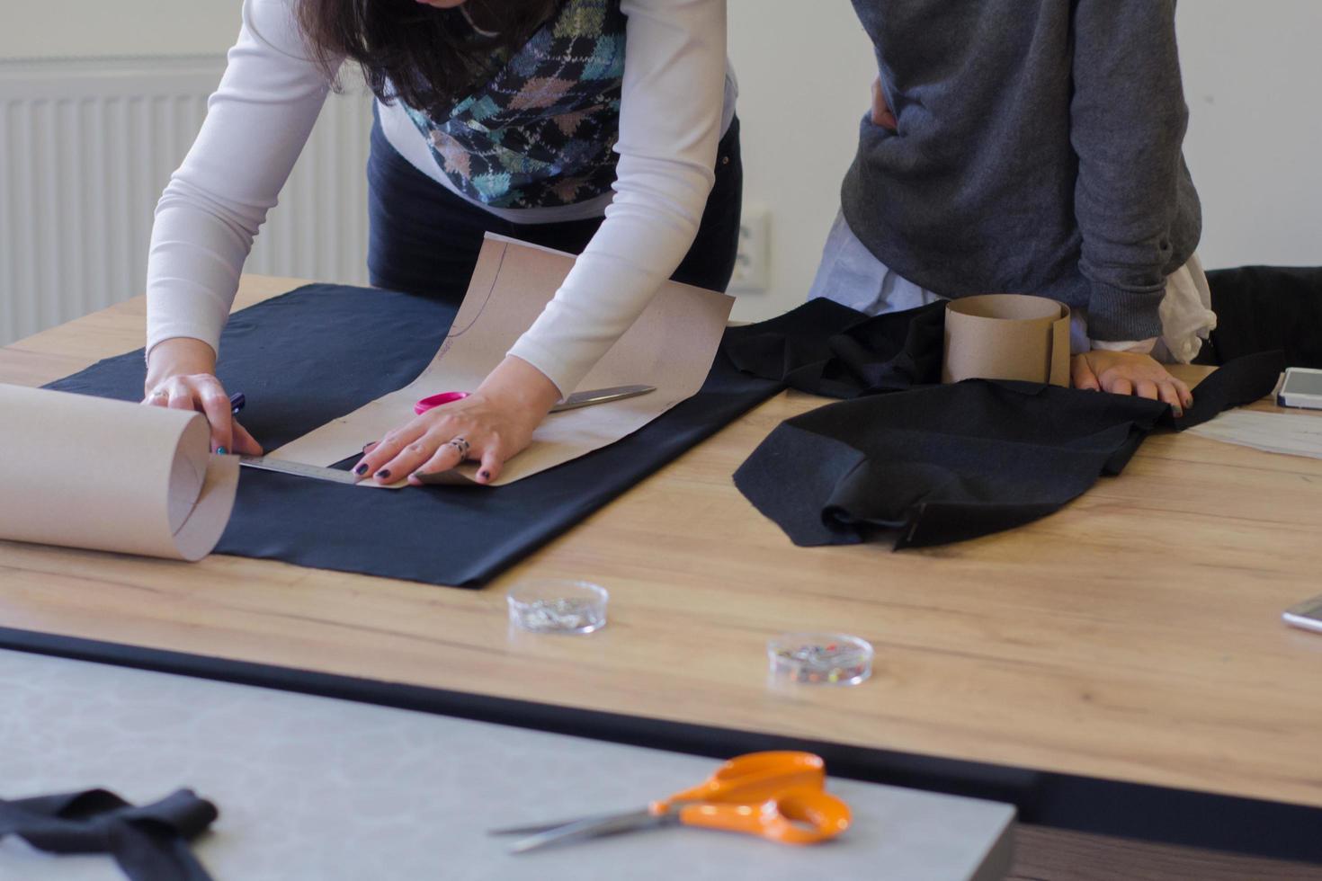 Näherin bei der Arbeit auf dem Tisch, Schneiderfrau arbeitet im Studio mit Kleidung foto