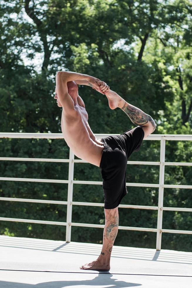 junger Mann mit Tätowierungen macht Yoga-Übungen im Freien auf dem Balkon foto