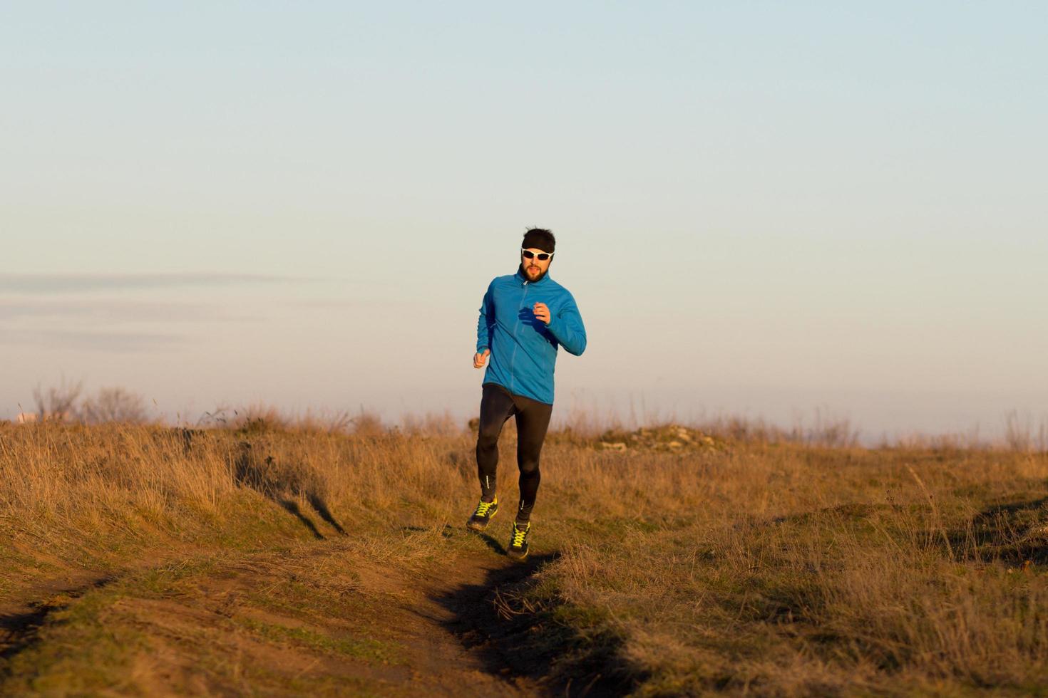 Junger Mann Trail Runner Training im Freien auf den Feldern, Sonnenuntergang im Seehintergrund foto