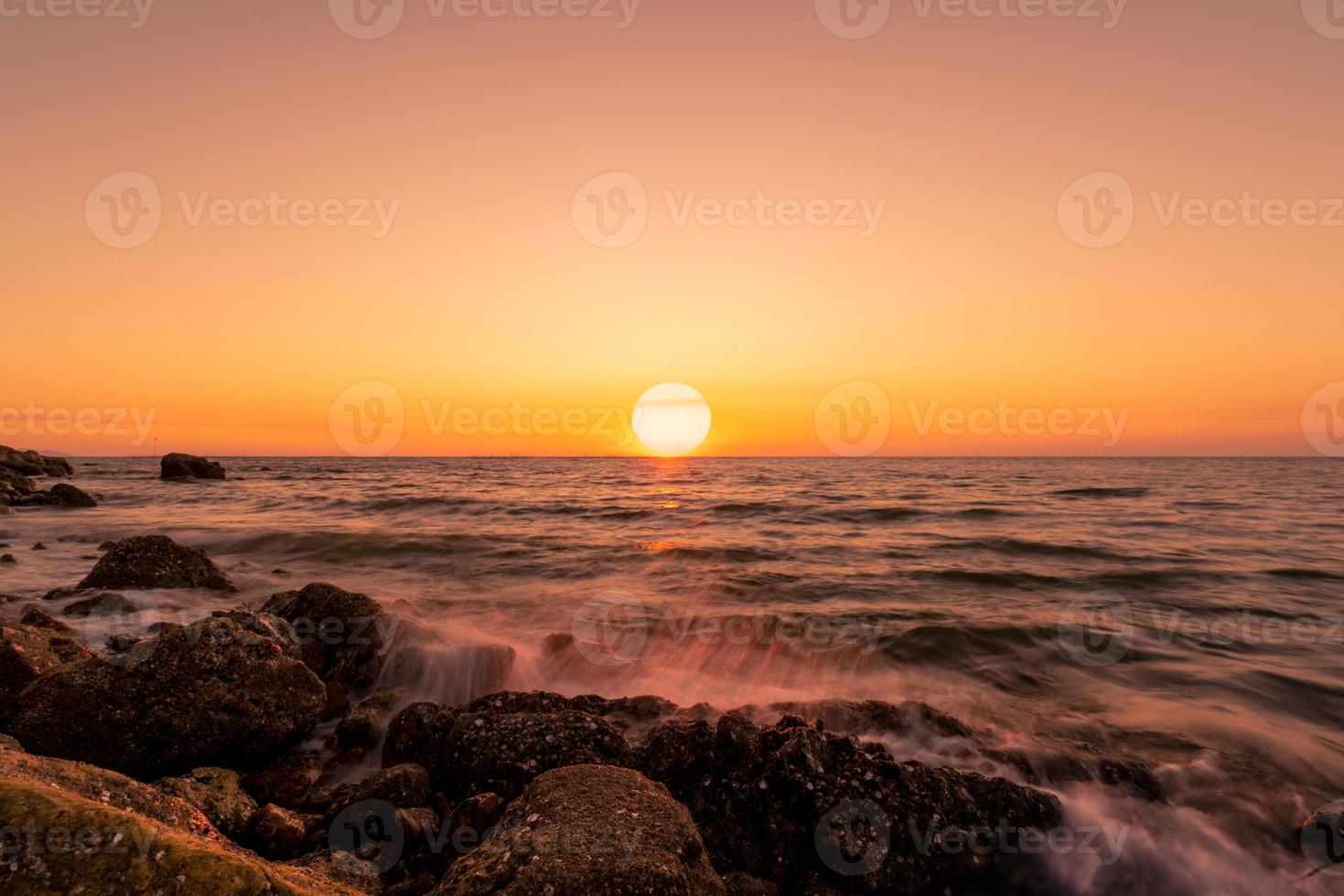 große sonne auf der skyline bei sonnenuntergang. ozeanwasserspritzer am felsstrand mit schönem sonnenunterganghimmel und orangefarbenen wolken. meereswelle, die im sommer auf stein am meer spritzt. Naturlandschaft. tropische Meereslandschaft. foto