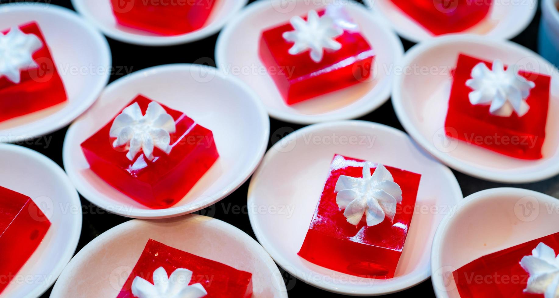 Rotes Gelee-Dessert mit Schlagsahne, serviert auf weißem Teller. Quadratisches rotes Gelee in Teller auf dem Tisch im Restaurant zum Mittagsbuffet. Süßes Essen. Gelee-Agar. dessertbuffet-catering-konzept, selektiver fokus. foto