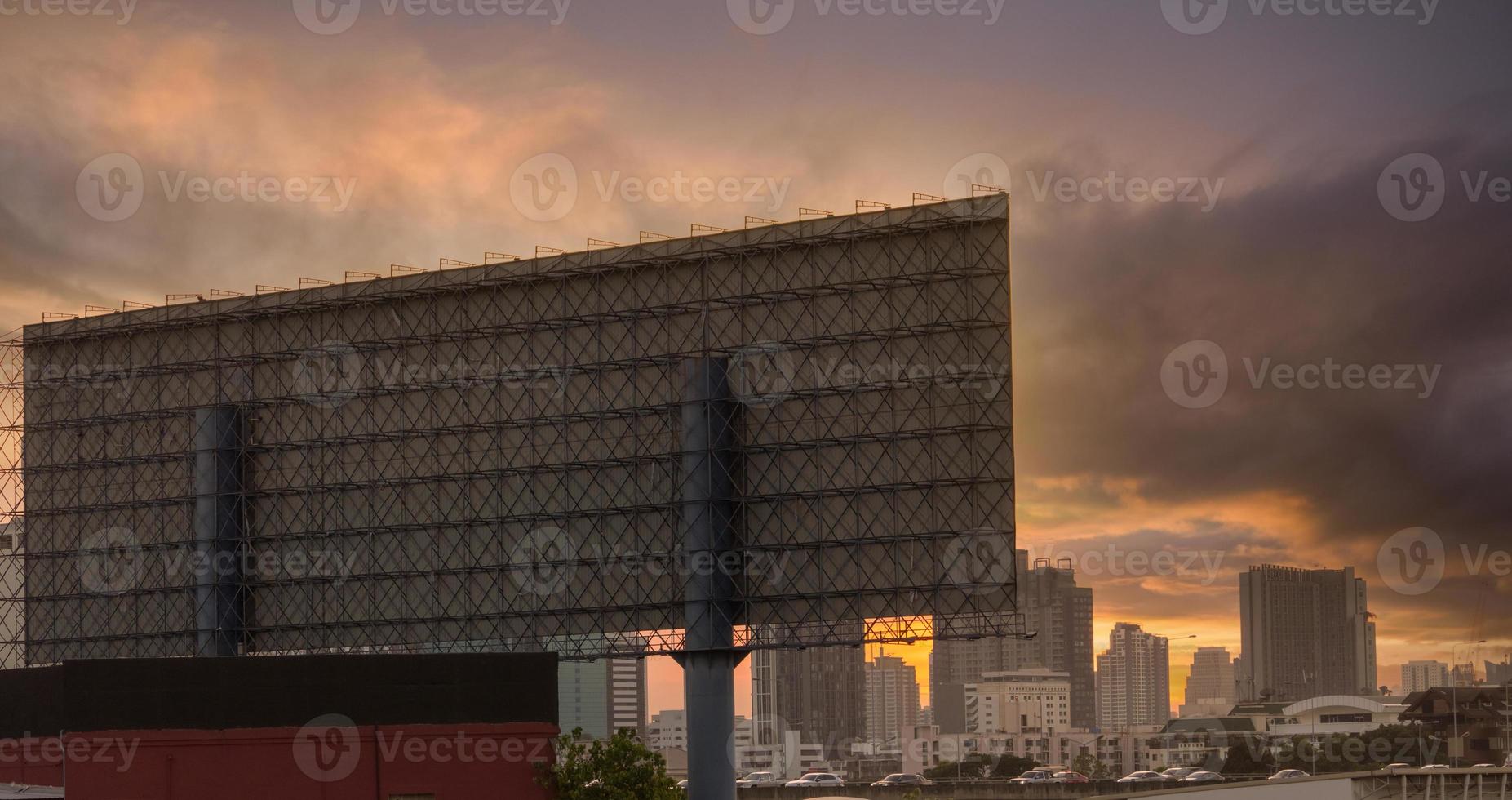 Stadtbild. Stadt am Abend. Ansicht von hinten Metallstruktur der Werbetafel. Hochhaus-Bürogebäude und Apartmentgebäude in der Hauptstadt mit Sonnenuntergangshimmel. autofahren auf der straße mit stau foto