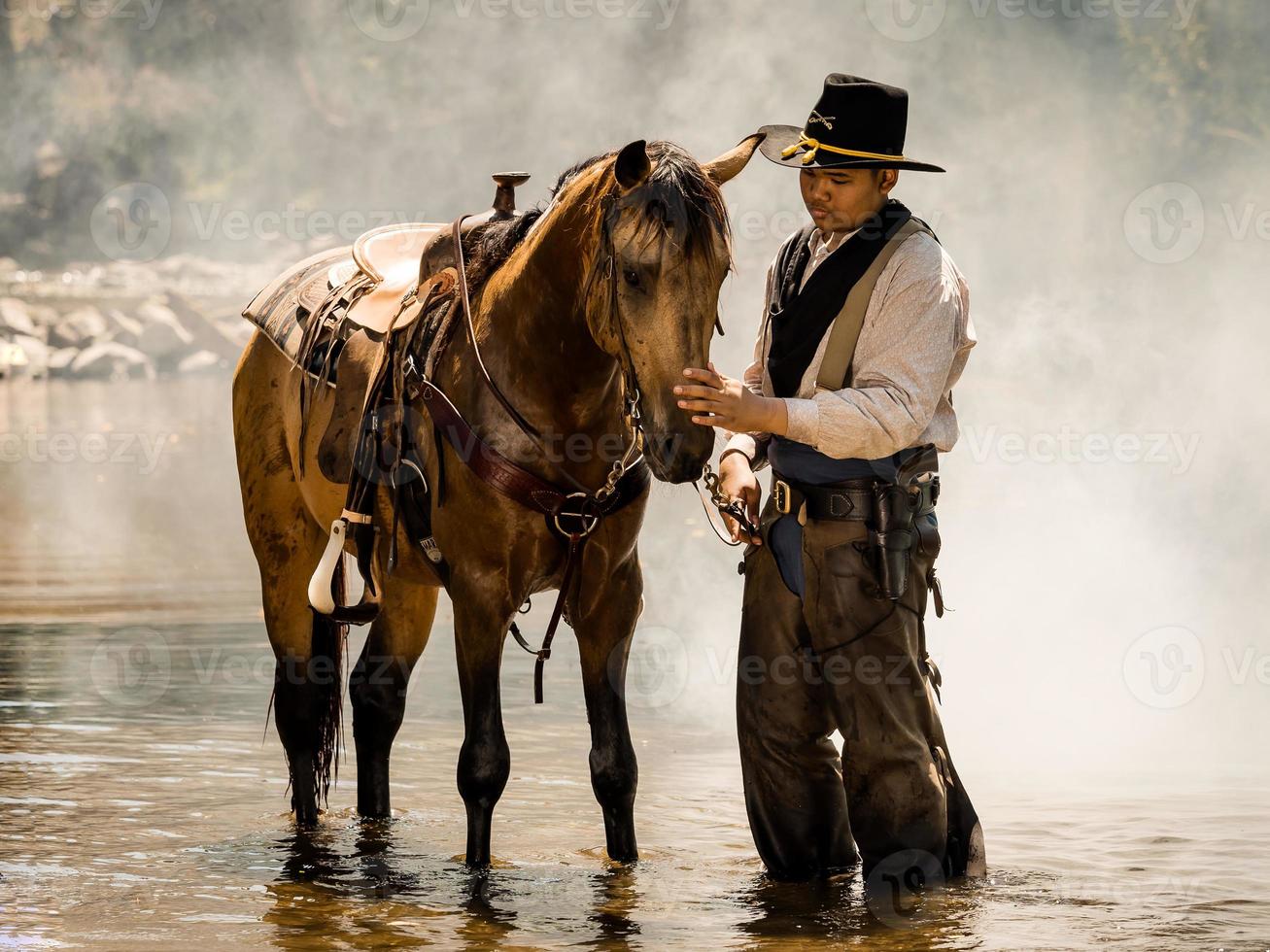 Ein junger Cowboy ruhte sich mit einem Pferd im Bach aus, nachdem er das Pferd geduscht hatte foto