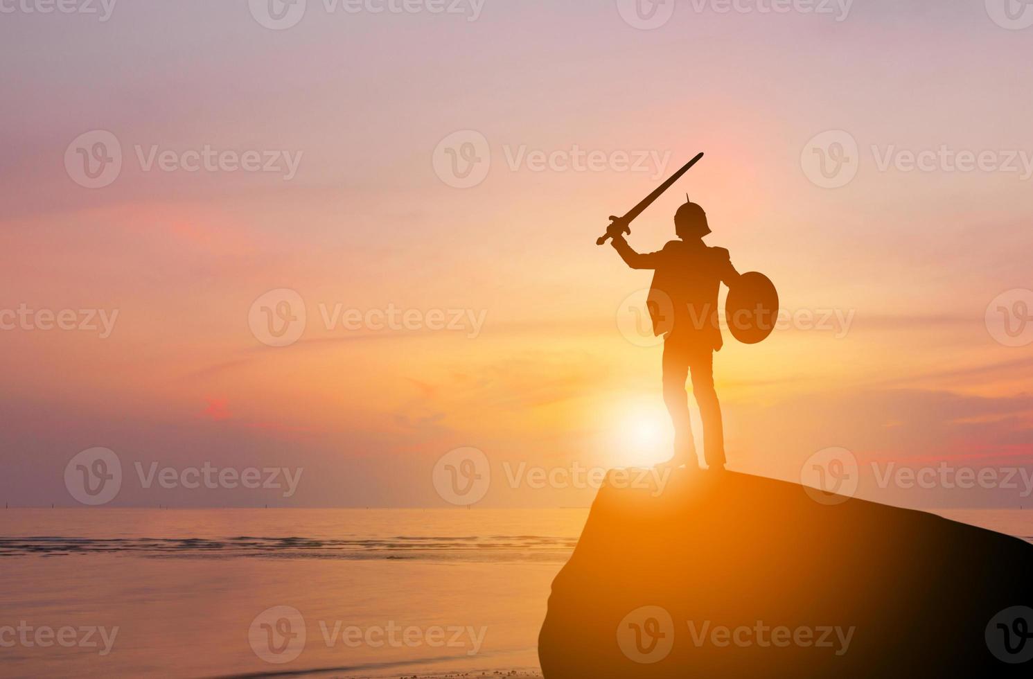 Silhouette des Geschäftsmannes, Ritterschwert und Schild im Sonnenuntergang, Kampf gegen das Geschäftskriegerkonzept. foto