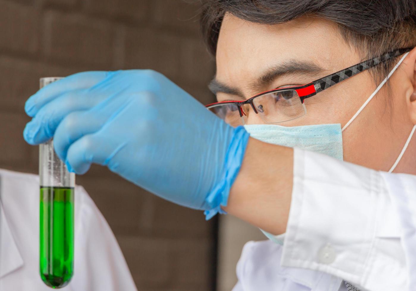 Nahaufnahme eines Wissenschaftlers, Mediziners, Arztes, der ein Reagenzglas mit Flüssigkeit in einem Labor betrachtet foto