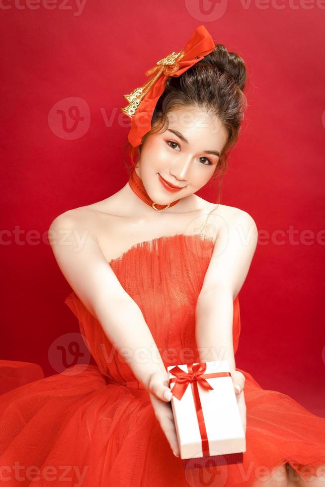 junges asiatisches hübsches frauenmodell in einem noblen stilvollen roten luxuskleid auf einem roten hintergrund lokalisiert. foto