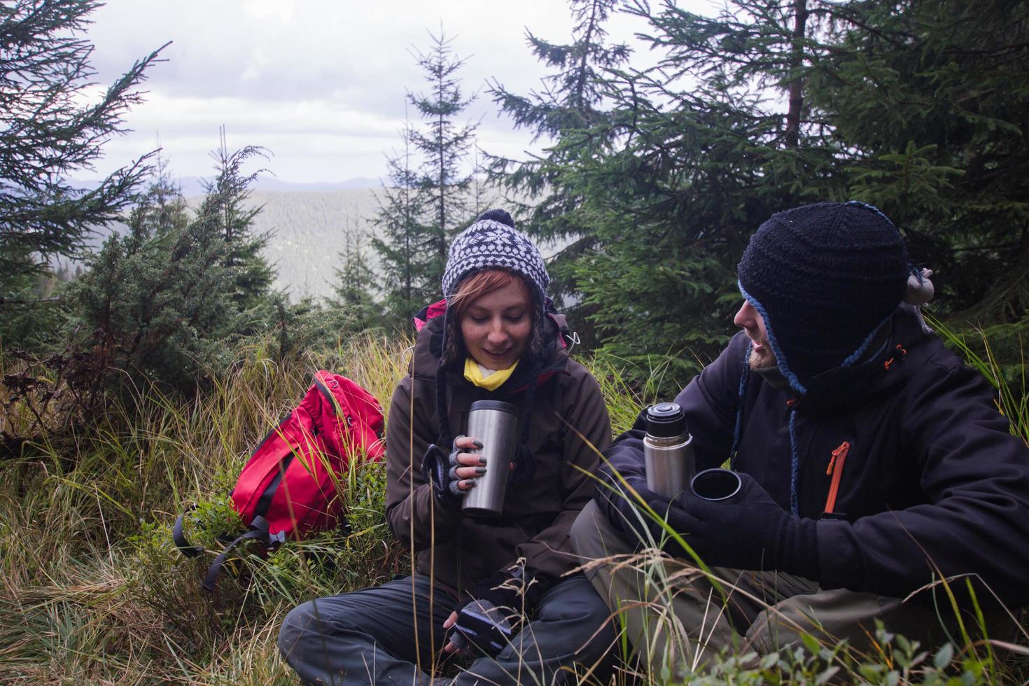 junges paar wanderer mit thermobechern im wald, reisende in den bergen, die tee oder kaffee trinken foto