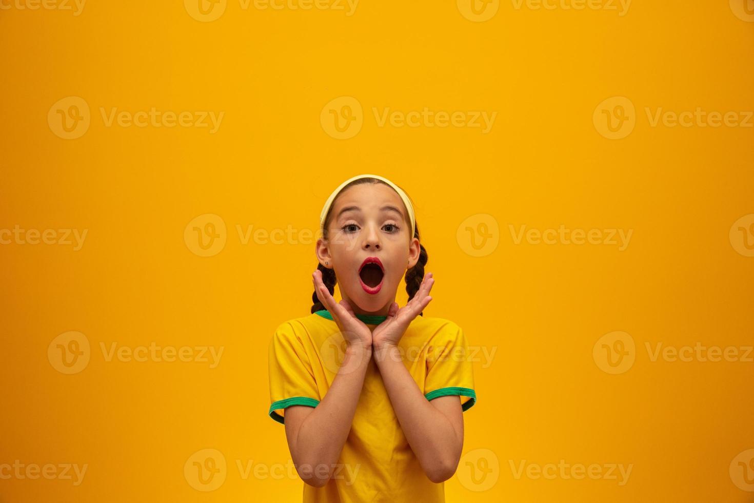 Fußballfan, brasilianische Mannschaft. Weltmeisterschaft. Schönes kleines Mädchen, das ihr Team auf gelbem Hintergrund anfeuert foto