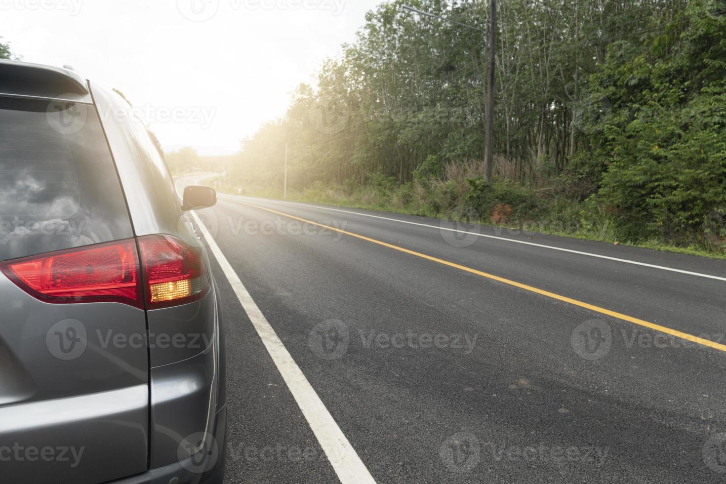 Auto, das auf der Asphaltstraße für die Reise einen geraden, gekrümmten Weg nach vorne fährt. mit grünem Wald neben der Straße. Rücklicht des Autos Licht einschalten signl. weiße Linie und die durchgezogene gelbe Linie auf der Straße. foto