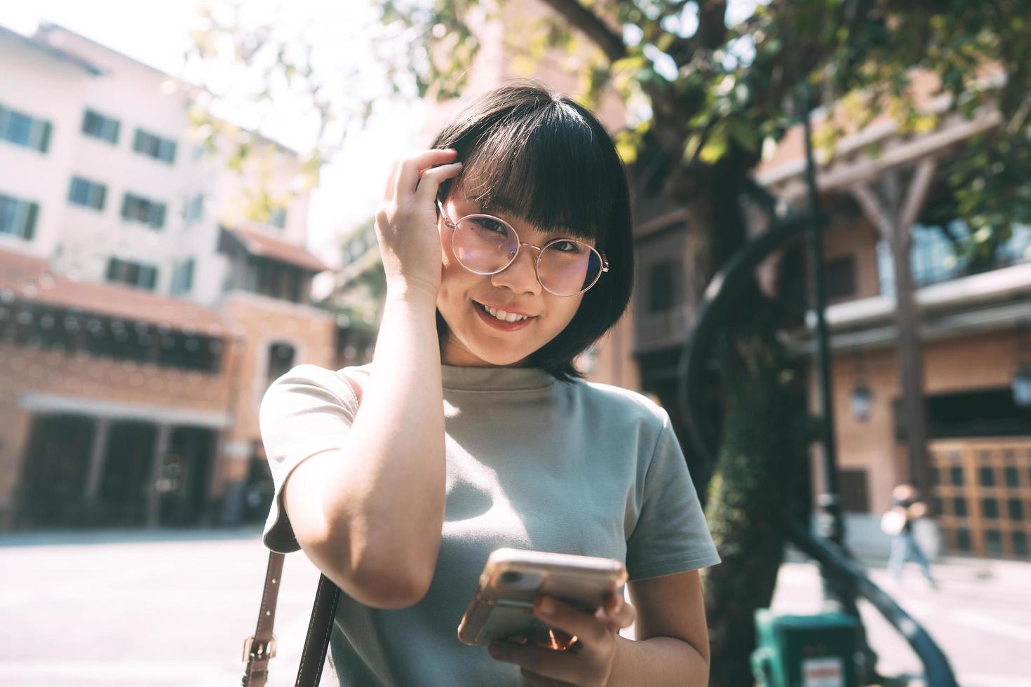 junge erwachsene glückliche asiatische frau trägt brillen mit handy für soziale medien. foto