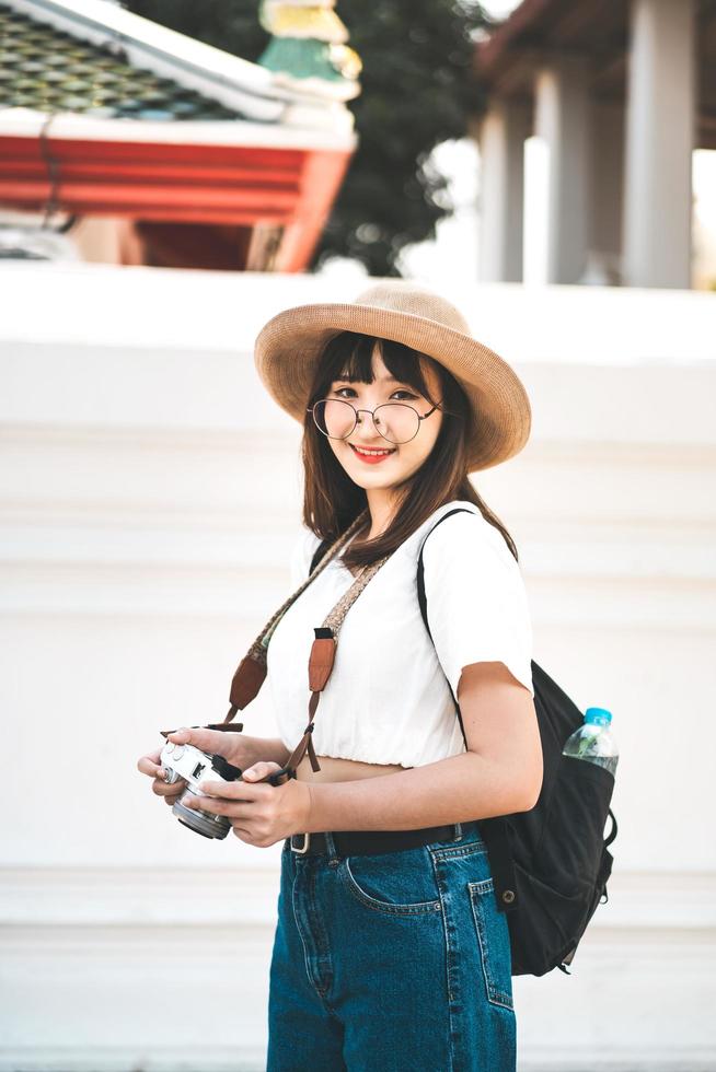 junges Mädchen mit asiatischem Einfluss, das mit Kamera und Rucksack in Bangkok reist. foto