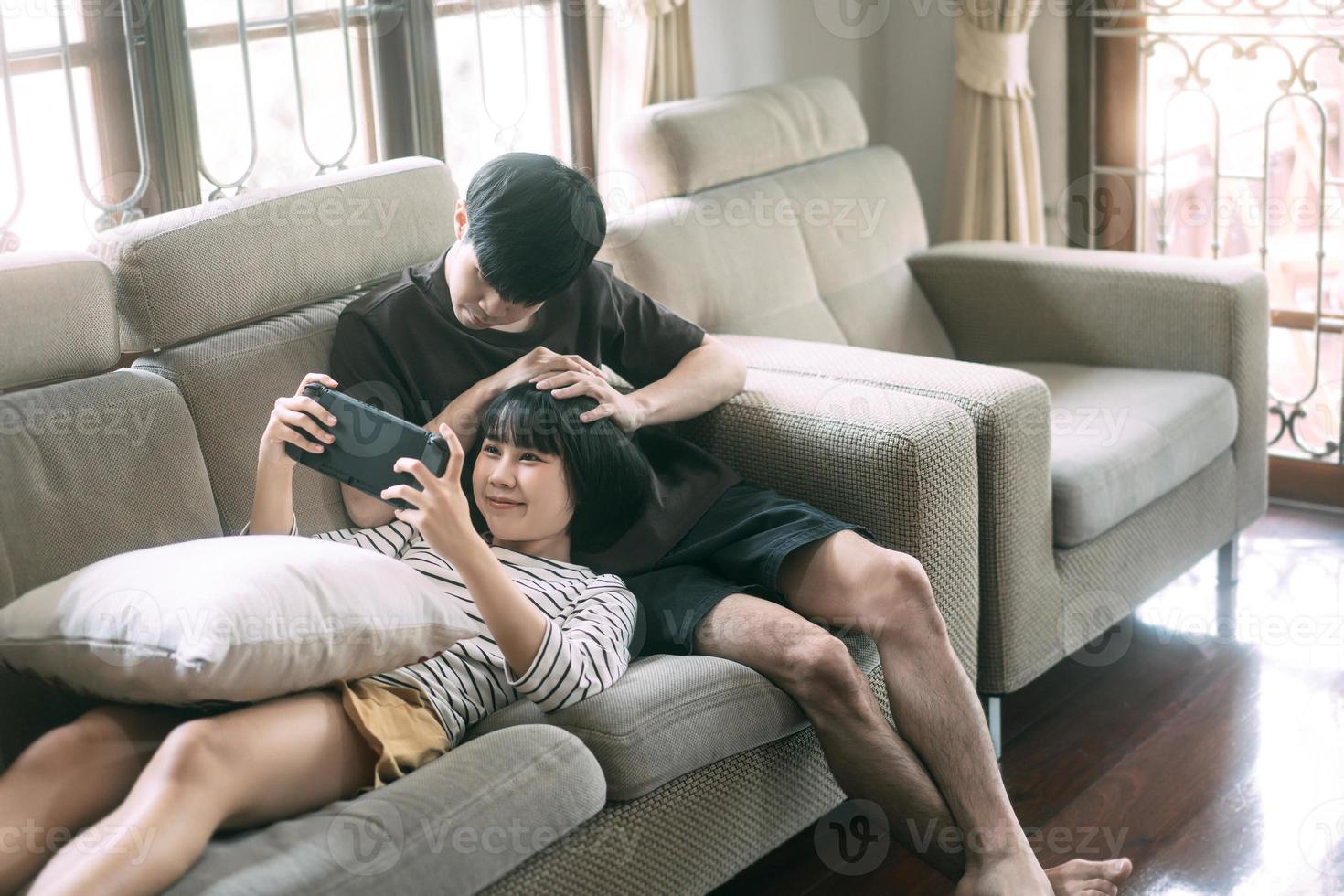 junges erwachsenes asiatisches liebhaberpaar, das auf dem sofa sitzt und am tag ein spiel im gemütlichen stil drinnen spielt. foto