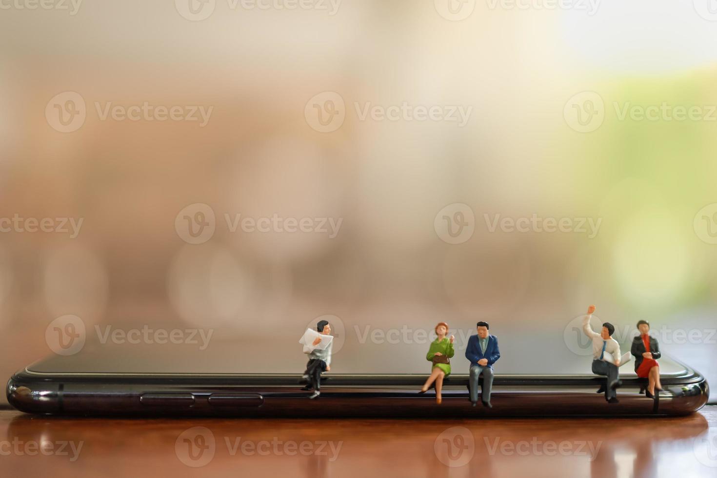 Geschäfts- und Kommunikationskonzept. nahaufnahme einer gruppe von geschäftsleuten und frauen miniaturfiguren, die auf einem intelligenten handy sitzen und mit einer zeitung mit kopienraum sprechen. foto