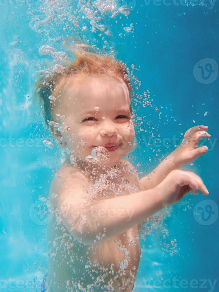 süßes, lächelndes, entzückendes Mädchen, das unter Wasser im blauen Pool taucht. aktiver lebensstil, kinderschwimmunterricht. Wassersportaktivitäten während der Sommerferien der Familie im tropischen Resort foto