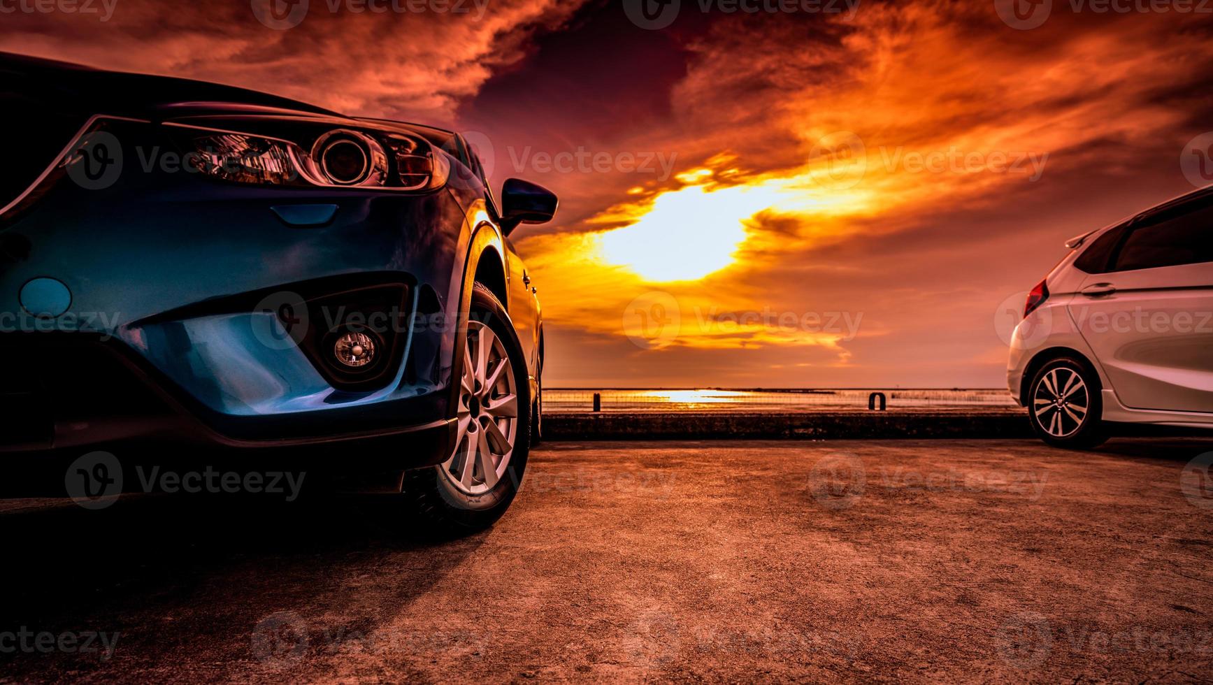 blau-weißer Kompakt-SUV mit sportlichem und modernem Design, der bei Sonnenuntergang auf einer Betonstraße am Meer in der Nähe des Strandes geparkt ist. umweltfreundliche Technologie. roadtrip auf urlaubsreise. foto