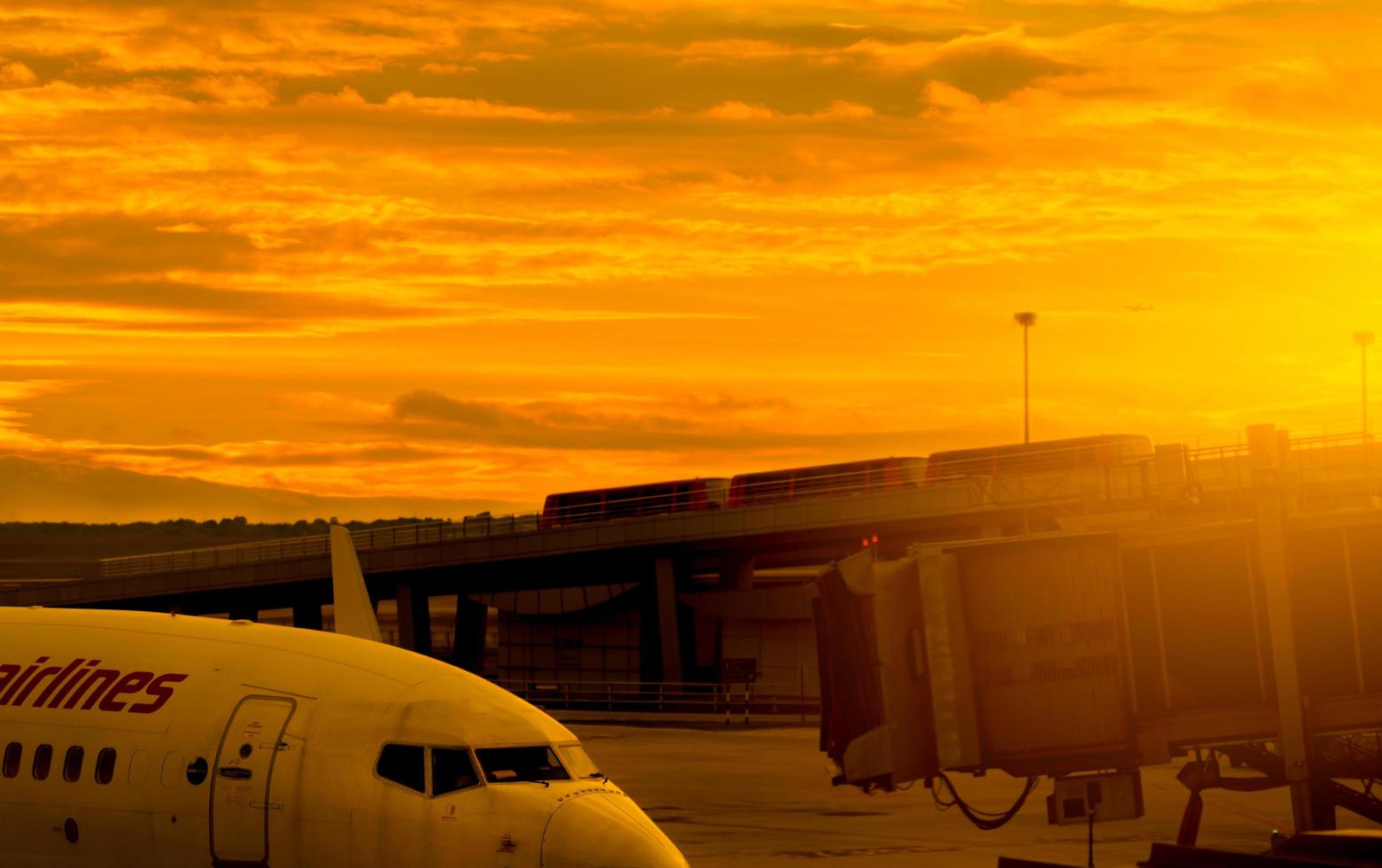 Verkehrsflugzeug, das an der Jet Bridge geparkt ist, um Passagiere am Flughafen abzuheben. Fluggastbrücke angedockt mit goldenem Sonnenuntergangshimmel in der Nähe der Straße. abflug der internationalen fluggesellschaft. foto