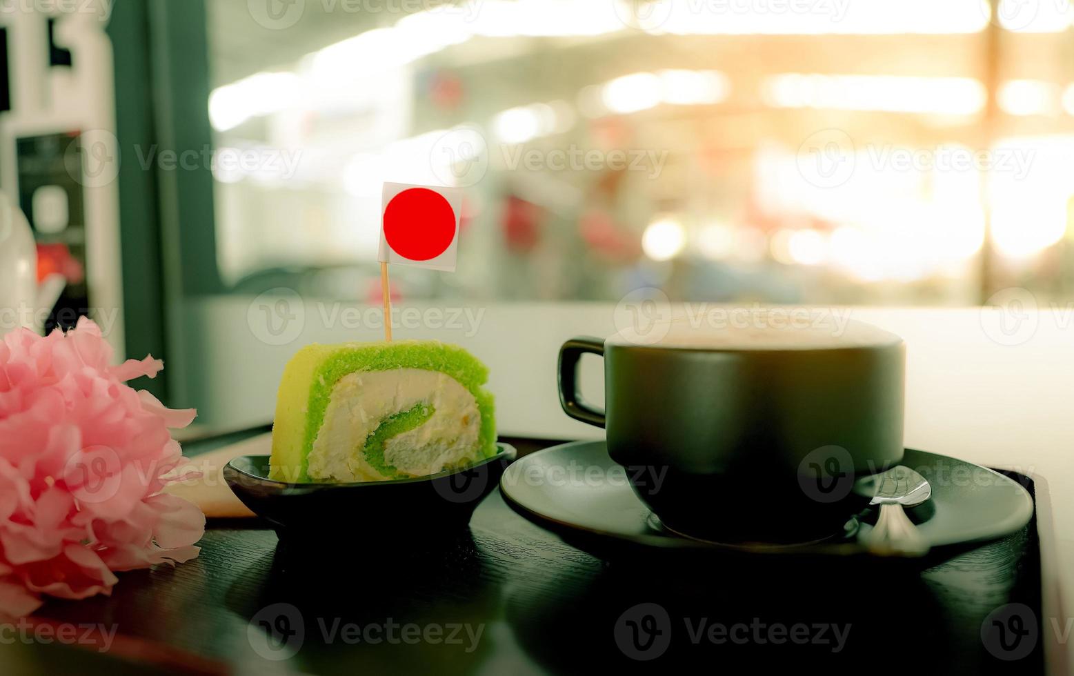 Heiße Kaffeetasse mit Stück grünem Schweizer Brötchenkuchen mit Sahne auf Teller im Café auf Holztablett im Café. Latte, Cappuccino oder Espresso im Glas. heisses Getränk. Koffeingetränk zum Frühstück foto