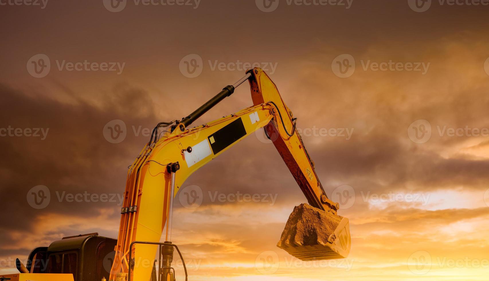 baggerarbeiten durch graben von boden auf der baustelle. Hydraulischer Arm und Baggerlöffel aus der Nähe mit einer Schaufel Erde gegen den gelben Sonnenuntergangshimmel. bagger, der auf schmutz gräbt. Grabenmaschine. foto