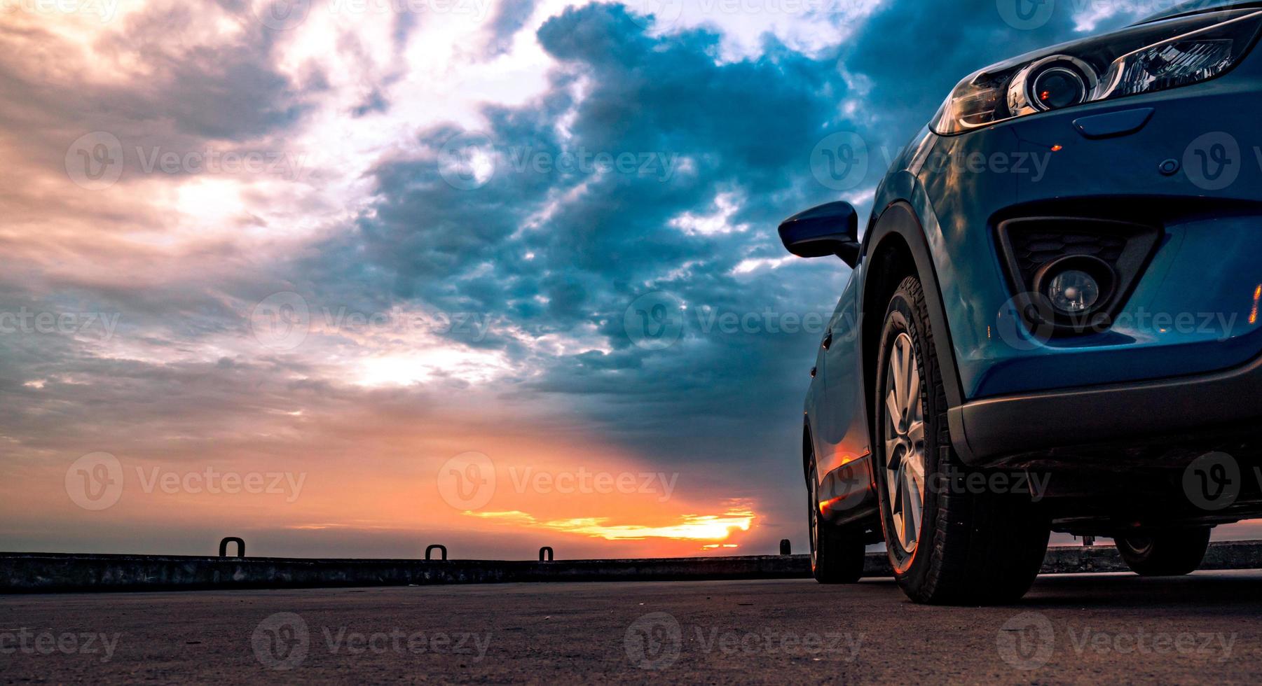 blaues kompaktes suv-auto mit sport und modernem design, das abends bei sonnenuntergang auf einer betonstraße am meer geparkt ist. hybrid- und elektroauto-technologiekonzept. Pkw-Stellplatz. Automobilindustrie. foto