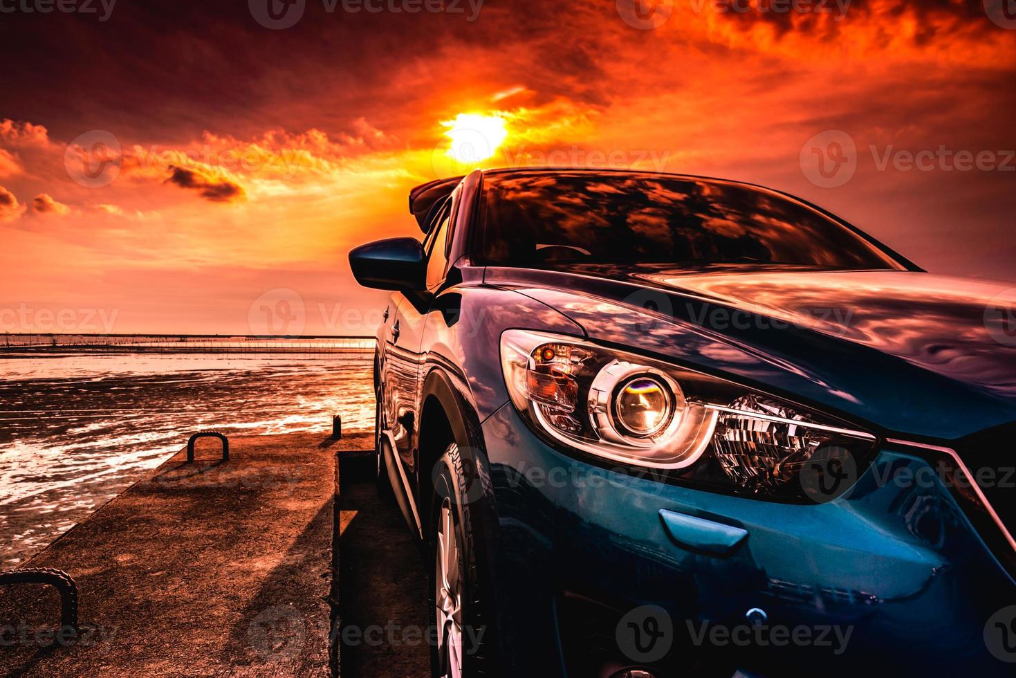 blaues kompaktes suv-auto mit sportlichem, modernem und luxuriösem design, das bei sonnenuntergang auf einer betonstraße am meer geparkt ist. Vorderansicht des schönen Hybridautos. fahren mit Zuversicht. Urlaub am Strand machen. foto