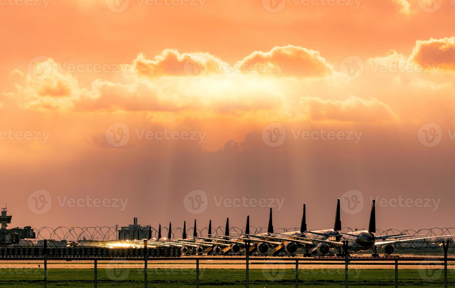 Verkehrsflugzeug, das nach den Auswirkungen der Coronavirus-Krise auf das Luftfahrtgeschäft auf dem Parkplatz des Flughafens geparkt wurde. Das Flugzeug ist innerhalb des Flughafenzauns mit Sonnenuntergangshimmel und grüner Rasenfläche geparkt. foto