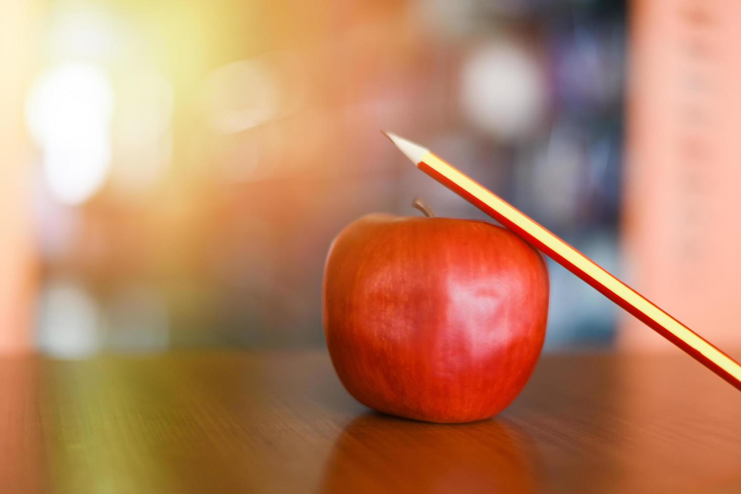 Bleistift auf einem Apfel auf dem Tisch in der Bibliothek - Bildungslernen auf Holzschreibtisch und verschwommenem Bücherregalraumhintergrund foto