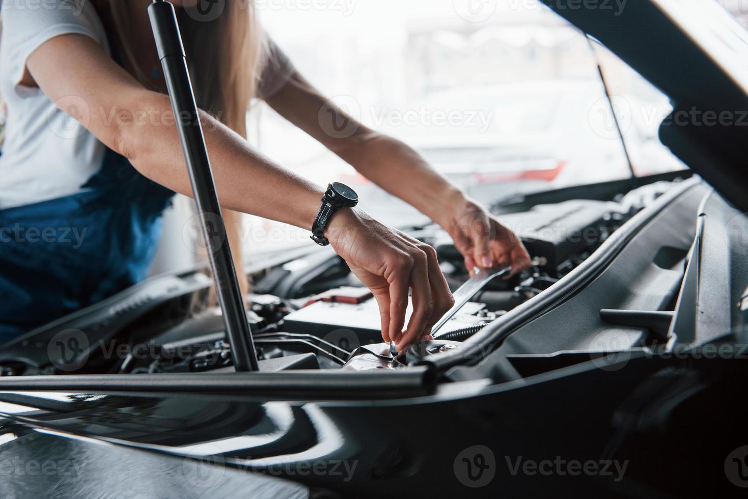 Einsetzen der Batterie. auf den schönen Job. autosüchtige frau repariert drinnen schwarzes auto foto