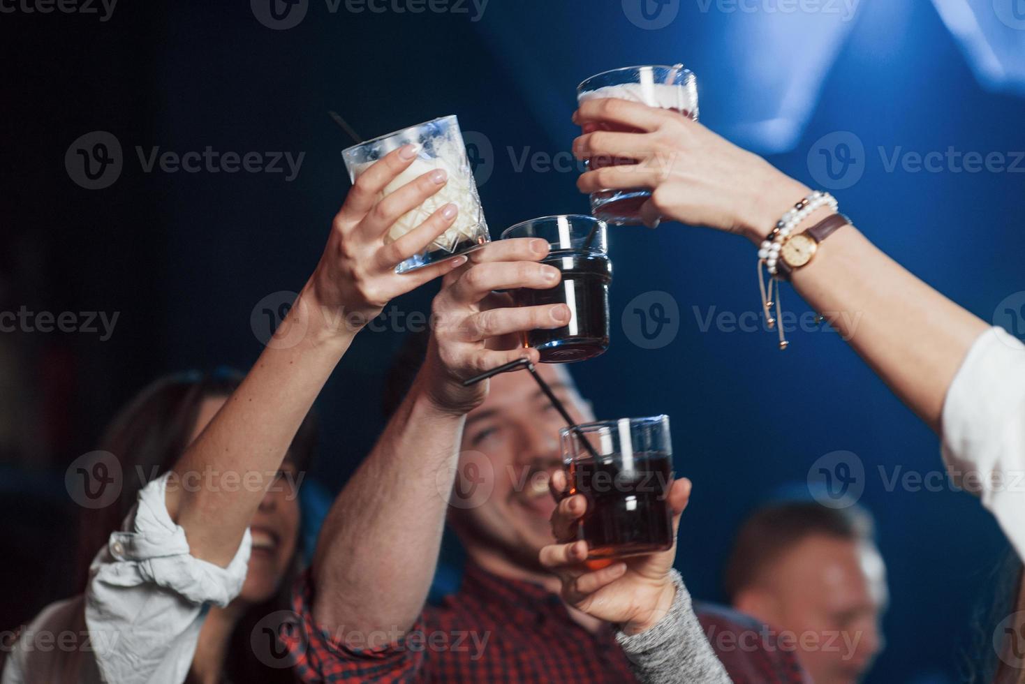 Lasst uns für unser Glück trinken. Gruppe junger Freunde, die im Nachtclub lächeln und anstoßen foto