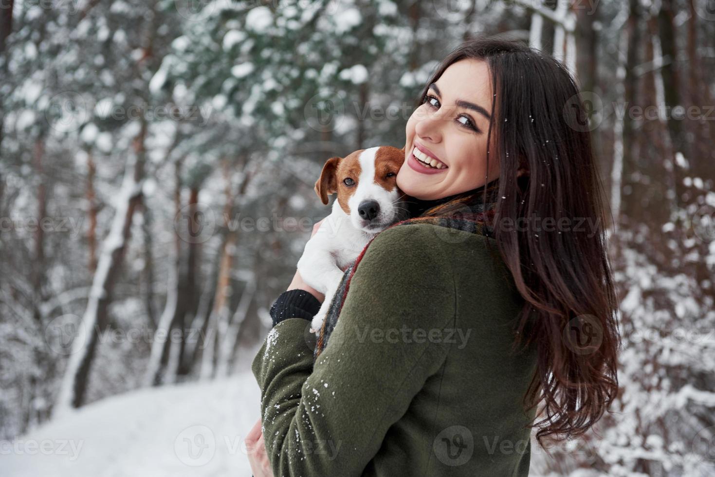 Mädchen dreht ihren Kopf zur Kamera. lächelnde brünette, die spaß hat, während sie mit ihrem hund im winterpark spazieren geht foto