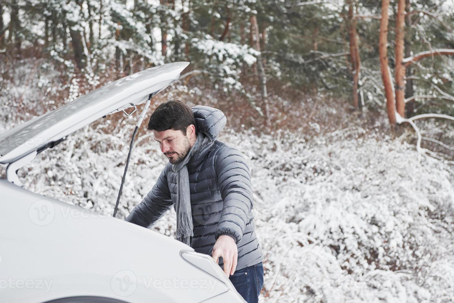 unerwartete Situation. Typ steckt im Winterwald fest, weil sein Auto Probleme hat. versucht, Auto zu reparieren foto