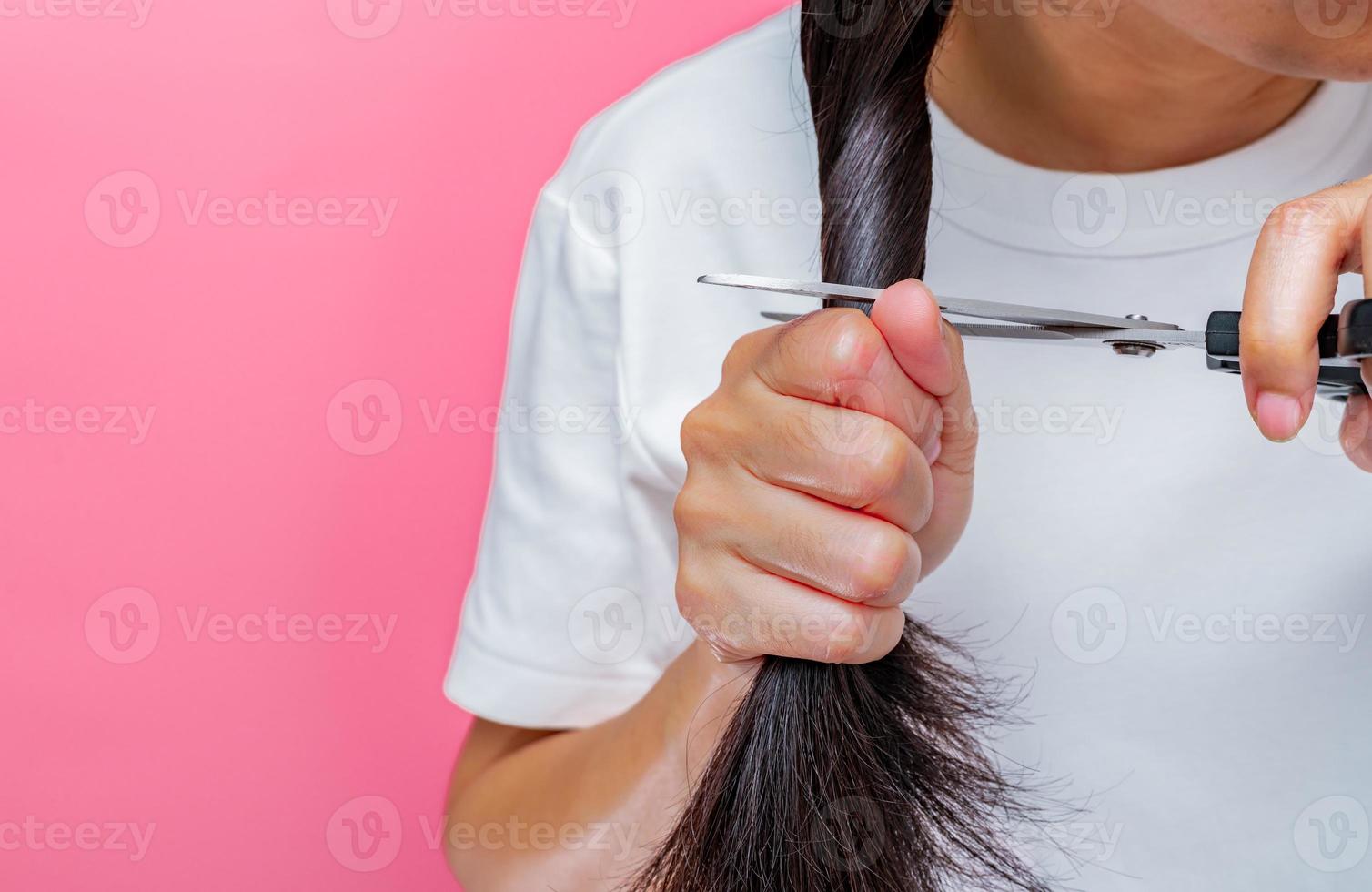 Frauen schneiden geschädigtes und trockenes Haar. asiatische frau, die haare mit einer schere schneidet, um an krebspatienten zu spenden. Haarspende für Brustkrebspatienten. frau mit schwarzen langen haaren auf rosa hintergrund. foto