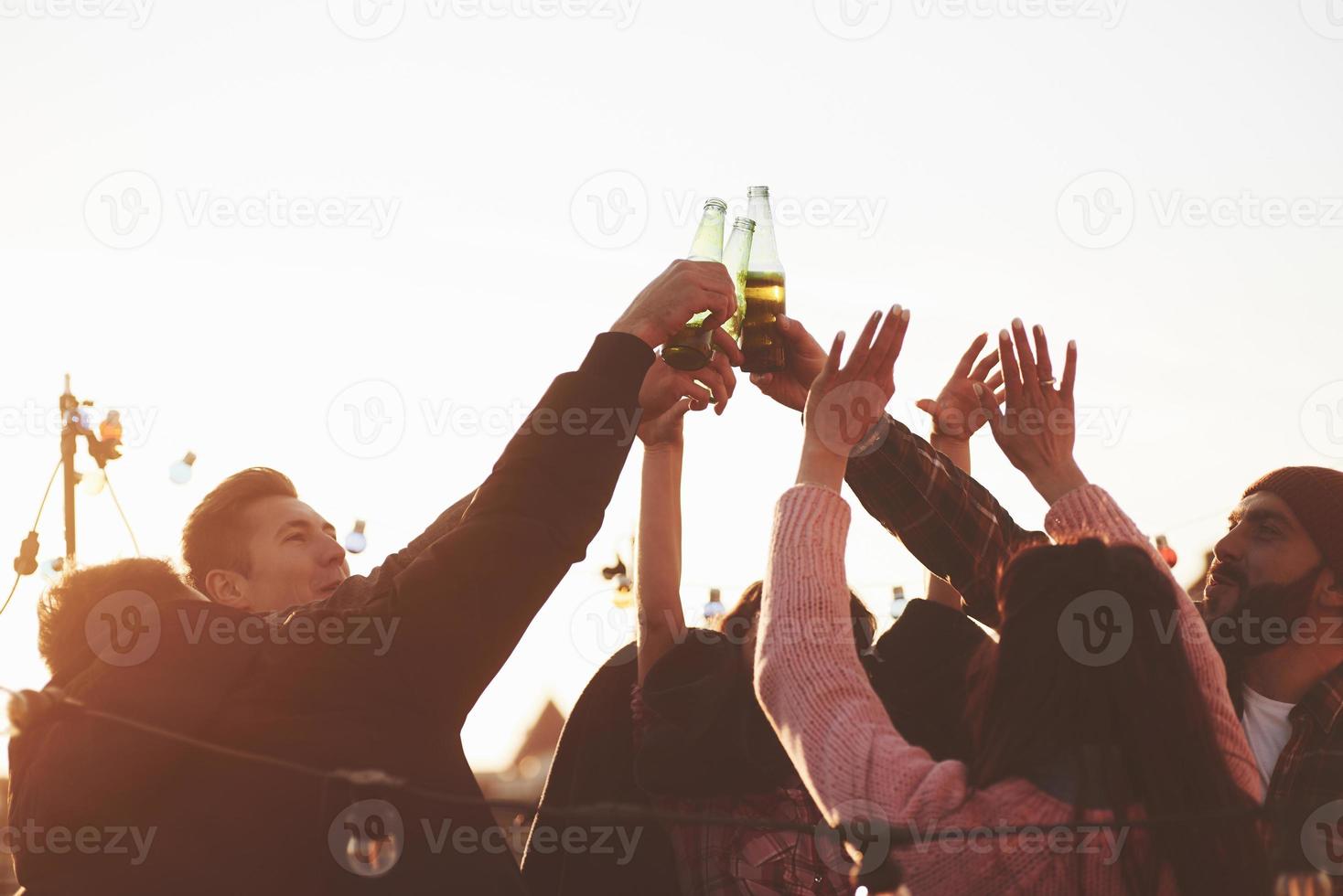 Flaschen auf. Urlaub auf dem Dach. Eine fröhliche Gruppe von Freunden hob die Hände mit Alkohol foto