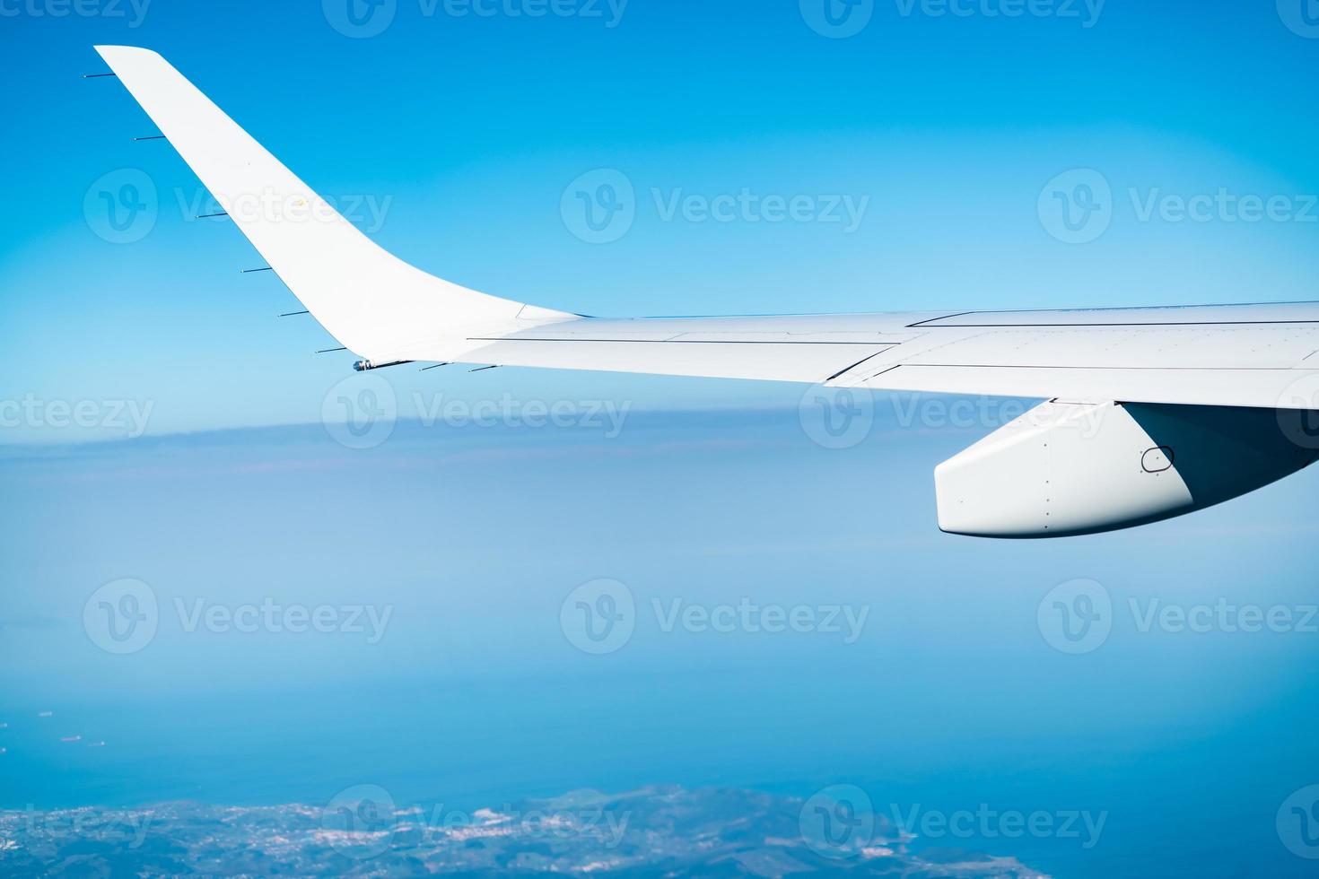 Flugzeugflügel über Stadt und Land. Flugzeug fliegt am blauen Himmel. malerische Aussicht aus dem Flugzeugfenster. Flug einer kommerziellen Fluggesellschaft. Flugzeugflügel über Wolken. Konzept der Flugmechanik. internationaler Flug. foto