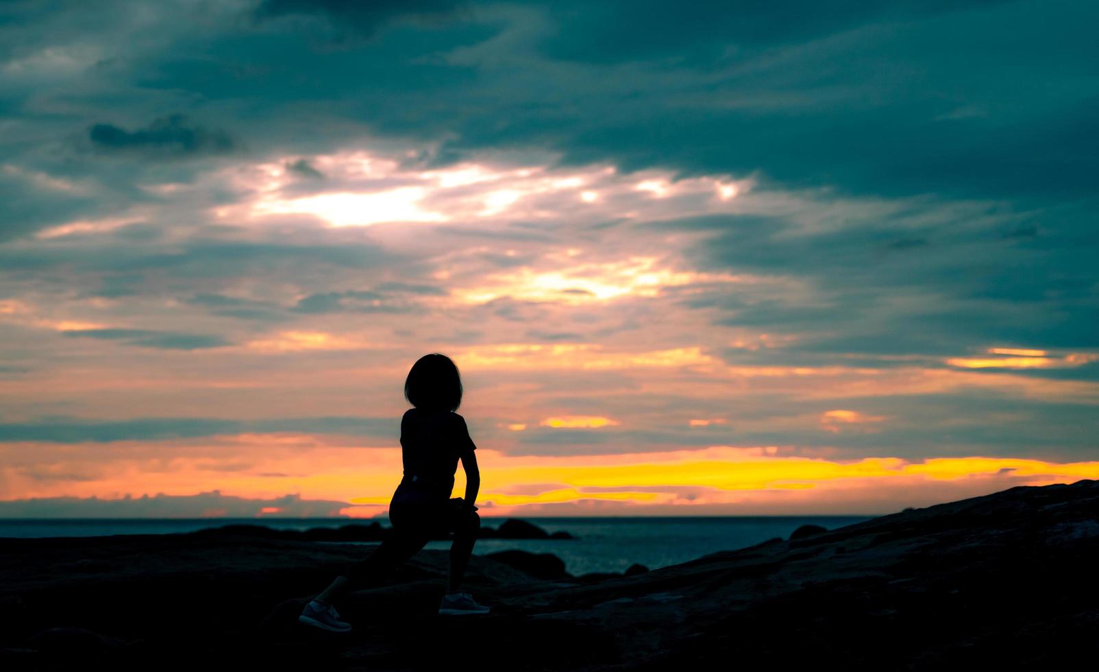 Silhouette Frau Training morgens am Steinstrand mit schönem Sonnenaufganghimmel. fitte frau, die körper vor dem training dehnt. Übung für einen gesunden Lebensstil. Training im Freien. Naturlandschaft. Freiheit foto