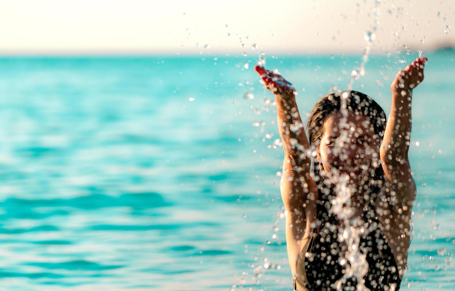 glückliche junge asiatische frau im schwarzen badeanzug entspannen und genießen urlaub am tropischen paradiesstrand. Mädchen im Sommerurlaub Spritzwasser im Meer. sexy Modell. sexy Frau im schwarzen Bikini. sommergefühl. foto