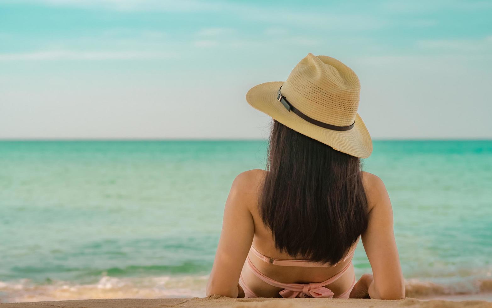 Rückansicht einer glücklichen jungen Asiatin in rosafarbenem Badeanzug und Strohhut Entspannen Sie sich und genießen Sie den Urlaub am tropischen Paradiesstrand bei Sonnenuntergang. Mädchen in der Sommerferienmode. Schönheit sexy Modell. sommergefühl. foto