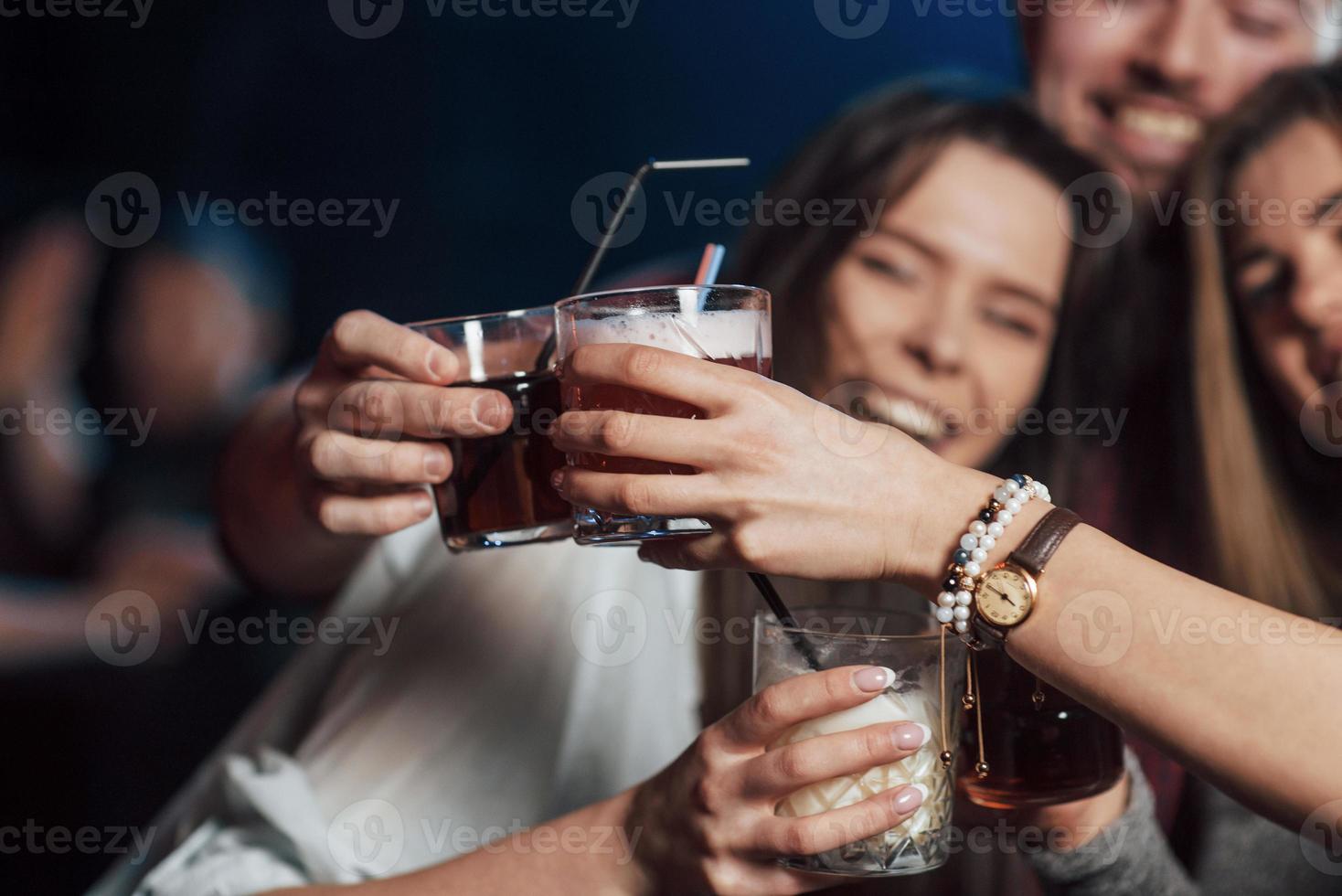 traditionelles Verfahren zum Klopfen von Gläsern. Gruppe junger Freunde, die im Nachtclub lächeln und anstoßen foto