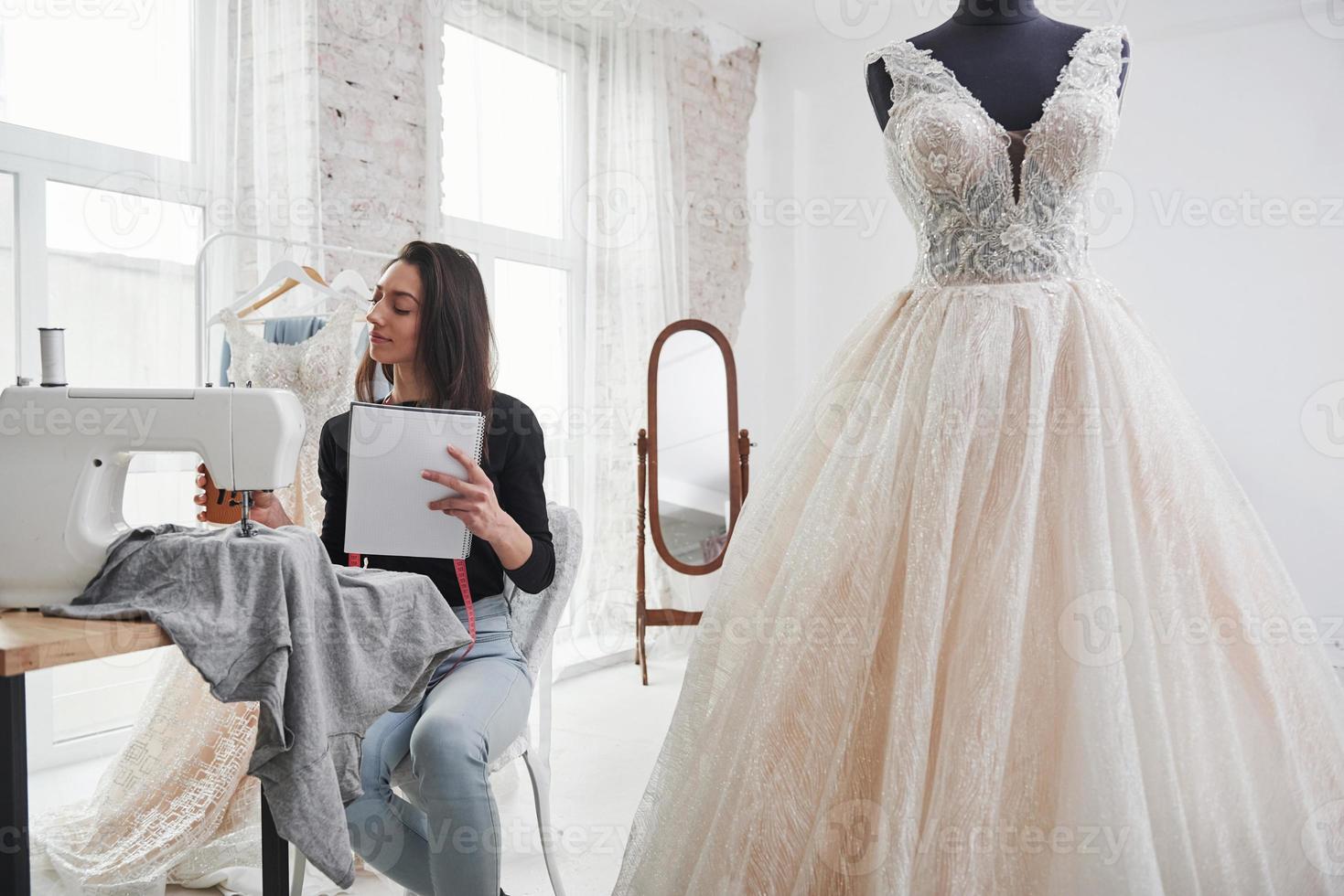 Tasse mit Getränk halten. Modedesignerin arbeitet in der Werkstatt an den neuen Kleidern foto