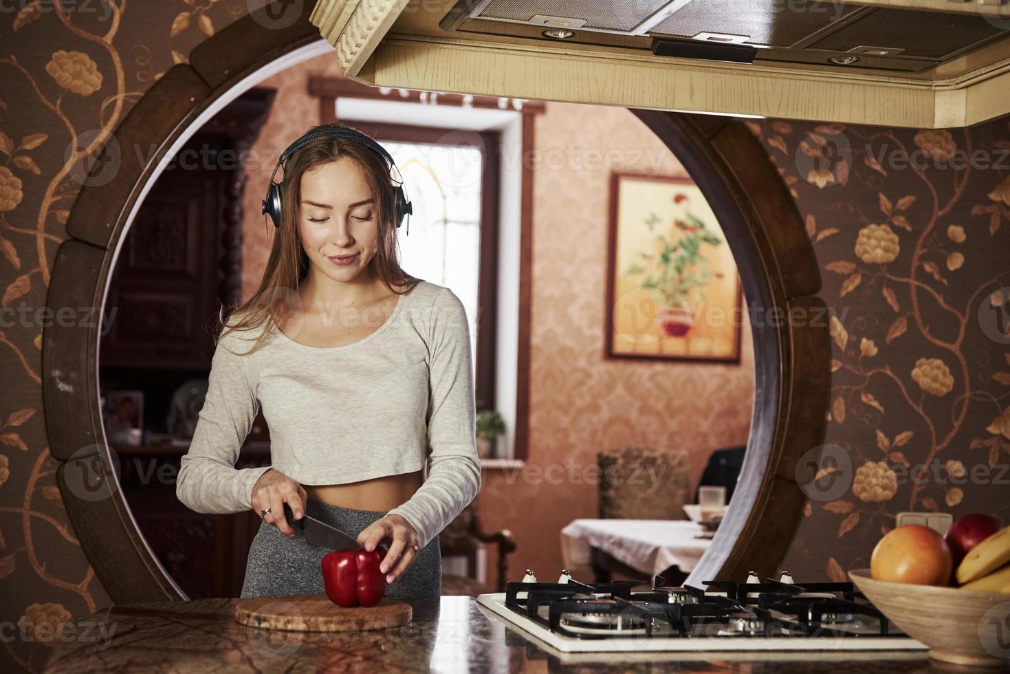 mit Messer, um Paprika zu schneiden. hübsche junge Frau, die in der modernen Küche in der Nähe des Gasherds steht und Essen zubereitet foto