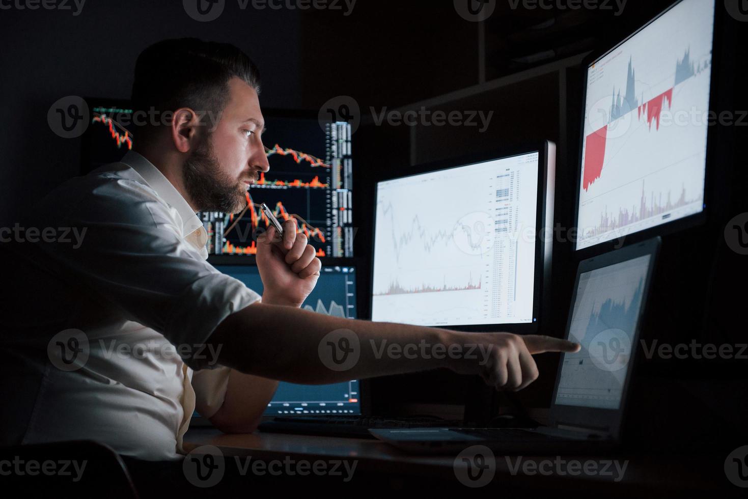 Zeigefinger in das Laptop-Display. bärtiger mann im weißen hemd arbeitet im büro mit mehreren computerbildschirmen in indexdiagrammen foto