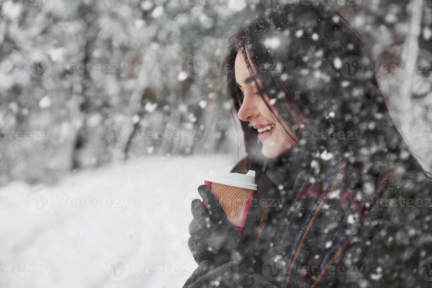 fallender Schnee im Wald. Mädchen in warmer Kleidung mit einer Tasse Kaffee spazieren im Winterwald foto