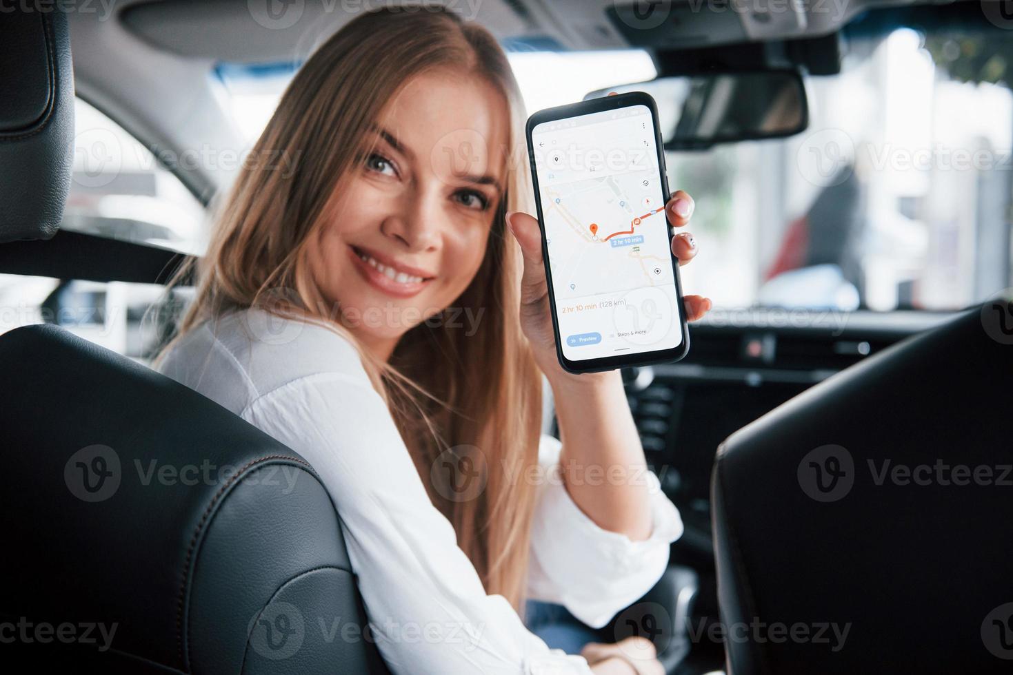 Strecke ist geschafft. schönes blondes mädchen, das im neuen auto mit modernem schwarzem interieur sitzt foto