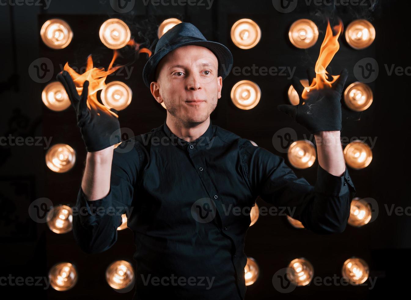 professioneller illusionist in schwarzem hut, hemd und glühen, die mit feuer spielen foto
