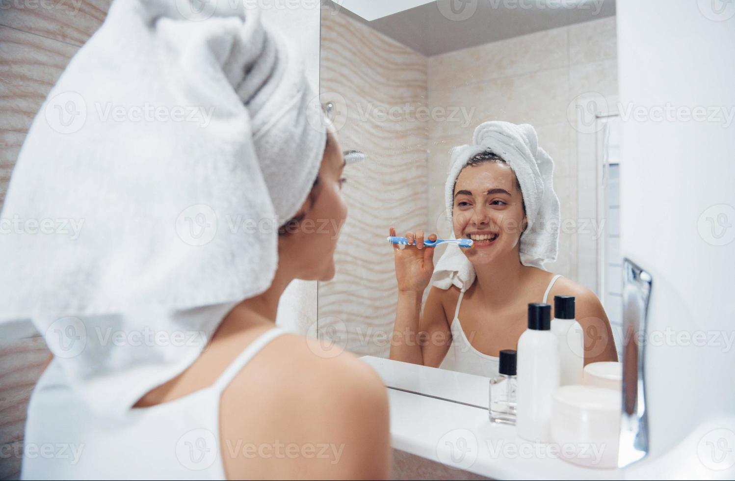 in den Spiegel schauen. im Badezimmer. frau im weißen handtuch im kopf passt auf sich auf foto