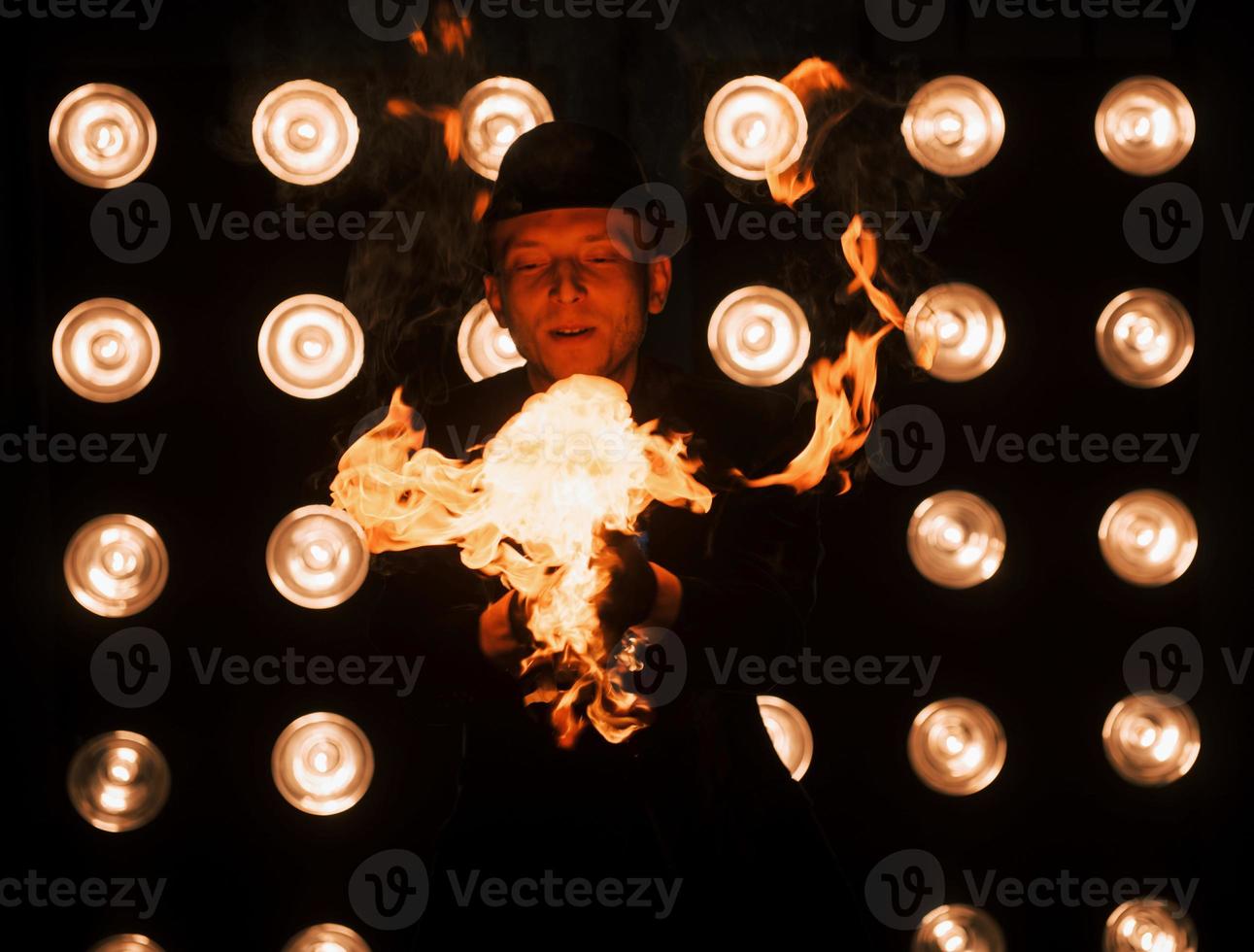 Die Kräfte der Natur sind in guten Händen. professioneller zauberer, der trick zeigt und mit feuer spielt. Glühbirnen im Hintergrund foto