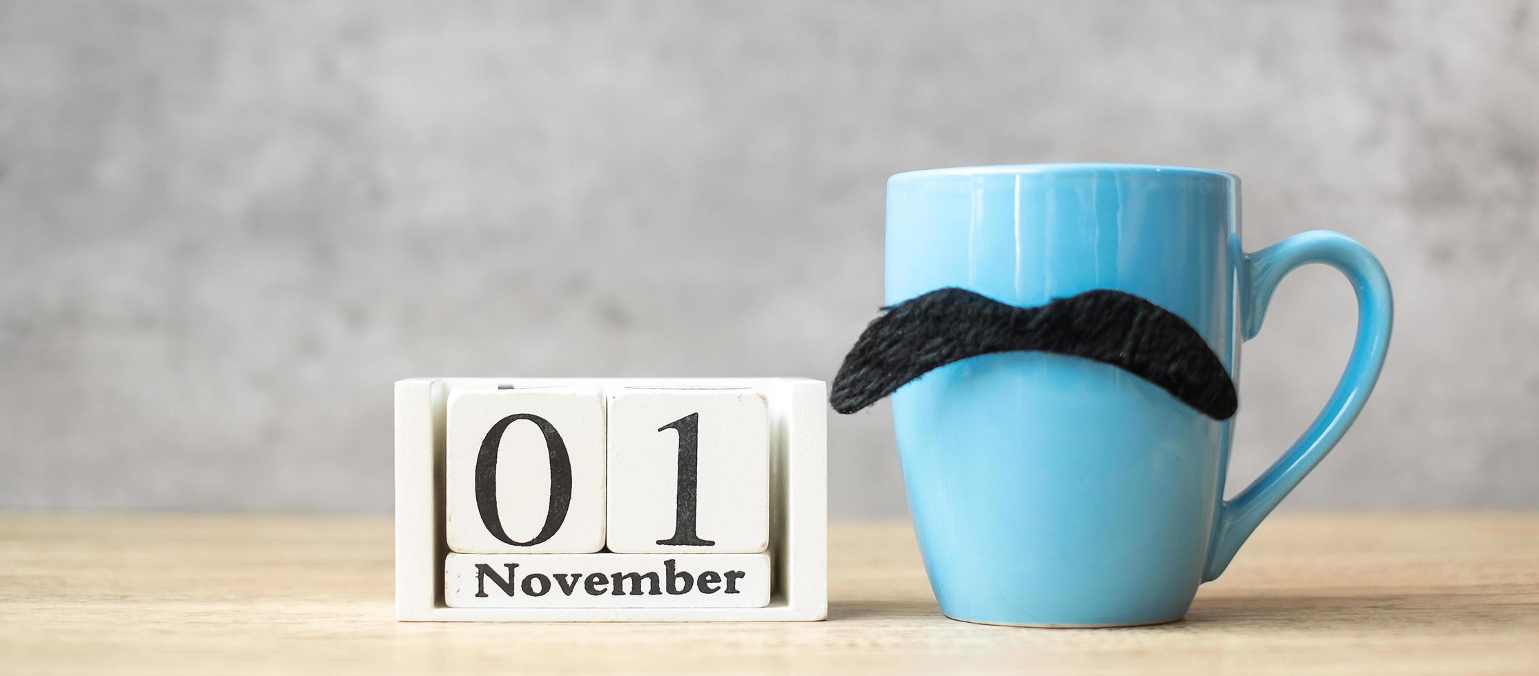 1. november kalender, blaue kaffeetasse oder teebecher und schwarzer schnurrbartdekor auf dem tisch. männertag, glücklicher vatertag und hallo november-konzept foto