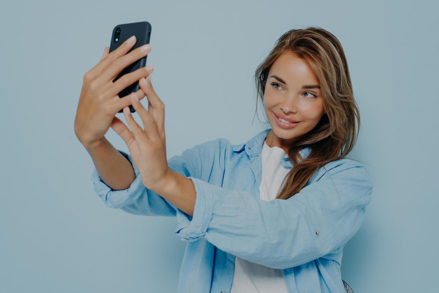 attraktiver blogger, der selfie nahe hellblauer wand macht foto