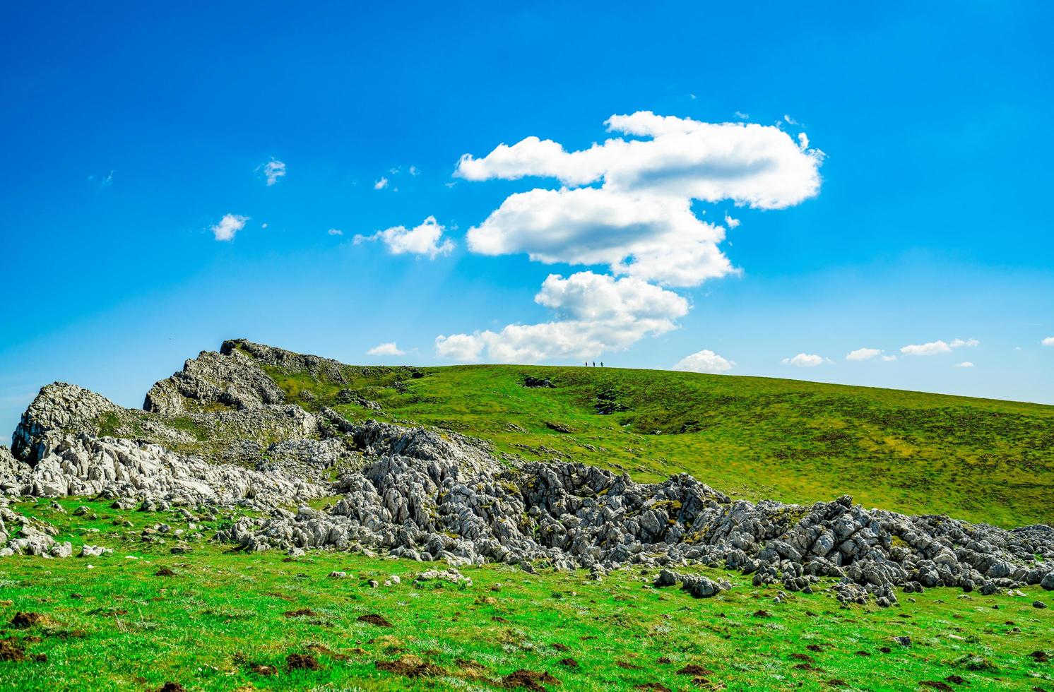 Landschaft aus grünem Gras und Felshügel im Frühling mit schönem blauem Himmel und weißen Wolken. Landschaft oder ländliche Aussicht. Naturhintergrund am sonnigen Tag. Frischluftumgebung. Stein auf dem Berg. foto